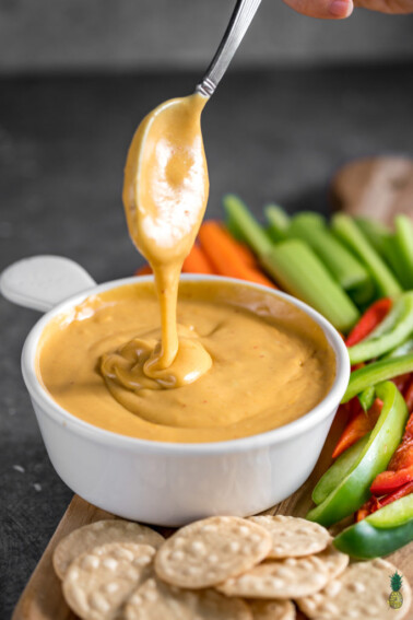 a spoonful of chipotle cashew cheddar cheese sauce being drizzled into the bowl