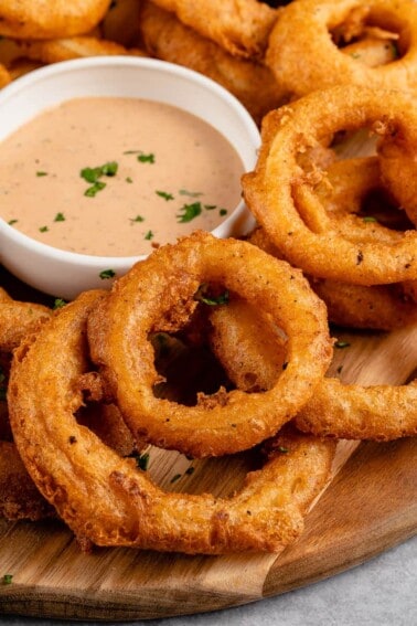 close up shot of vegan onion rings on a platter with dipping sauce