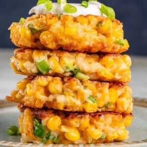 corn fritters in a stack on blue plate with mayo and scallions on top