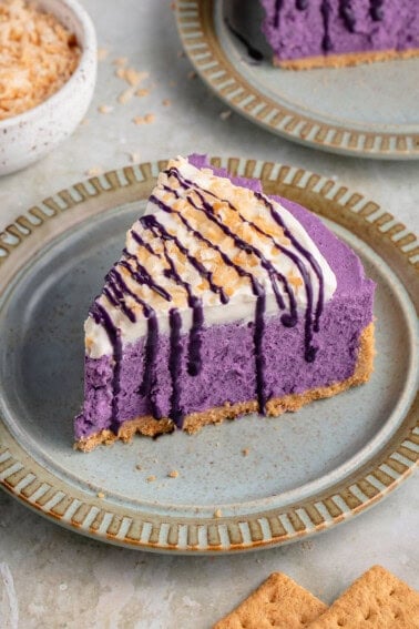 ube cheesecake on a blue plate surrounded by coconut flakes and graham crackers