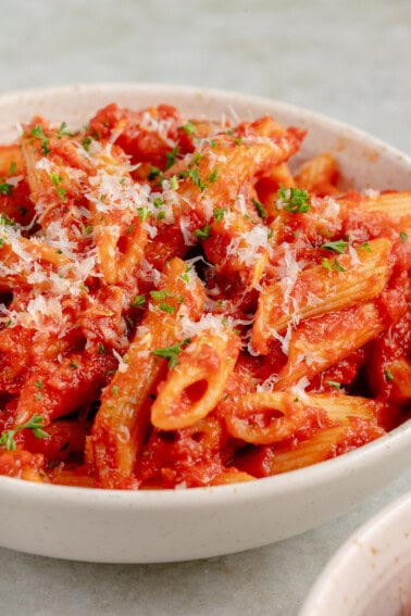 close up photo of Penne All'Arrabbiata (Spicy Tomato Pasta) with vegan parmesan and parsley in white bowl