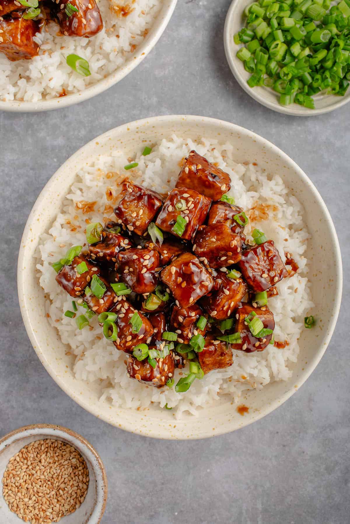 bowl of sticky sesame tofu on top of rice with green onions