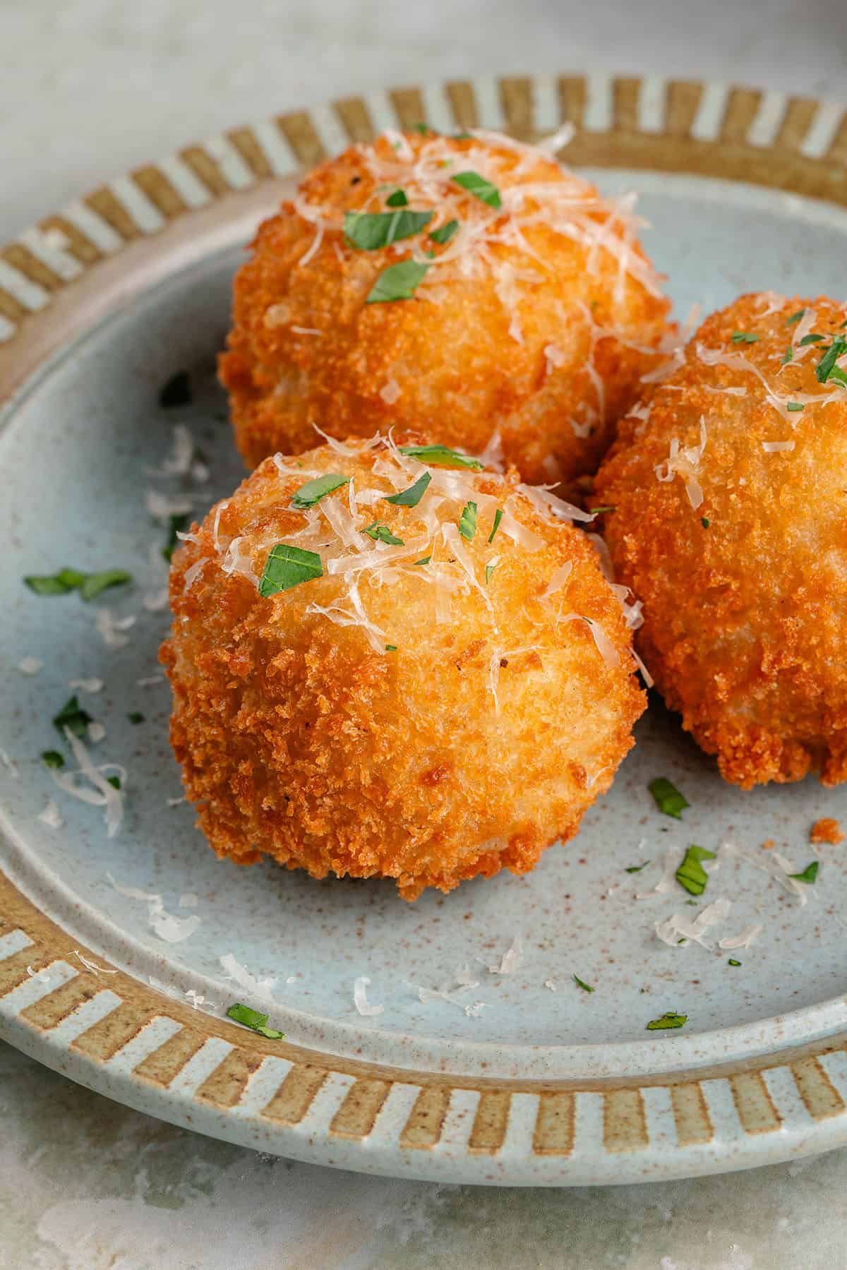 arancini on blue plate topped with parmesan and fresh parsley