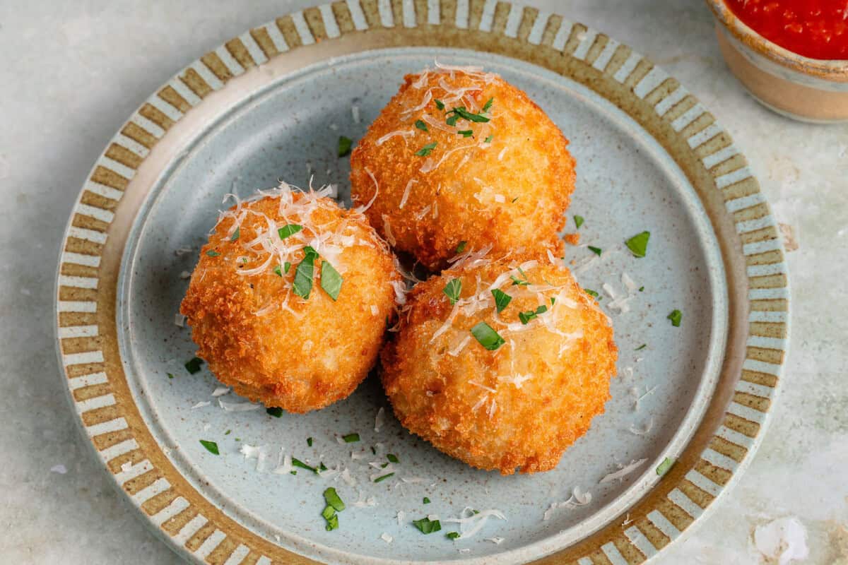 arancini on blue plate topped with parmesan and fresh parsley