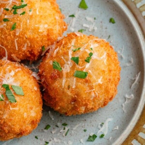 arancini on blue plate topped with parmesan and fresh parsley