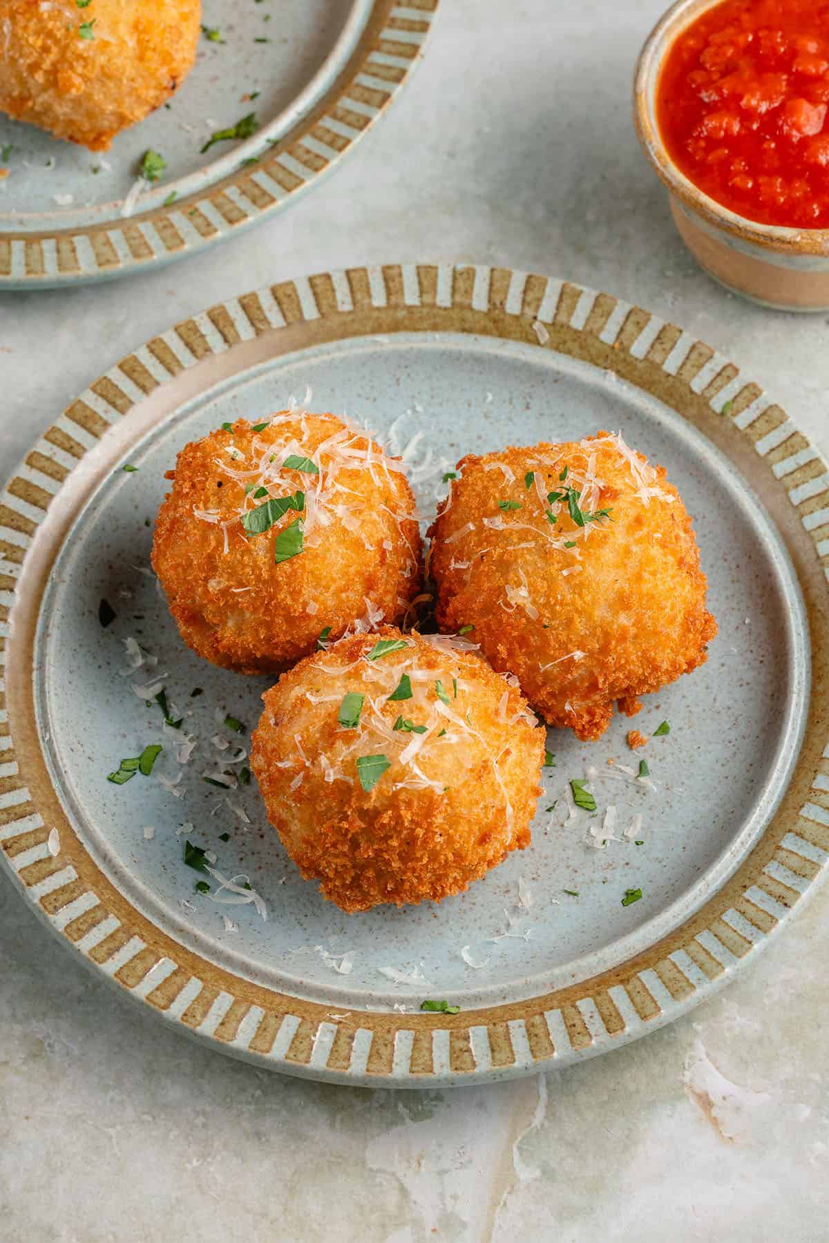 arancini on blue plate topped with parmesan and fresh parsley with a side of marinara