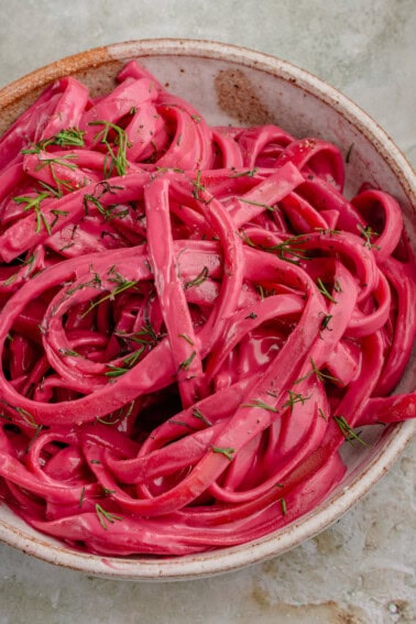 close up photo of bowl of creamy Vegan Beet Pasta sauce on fettuccine topped with dill