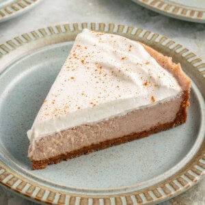 a slice of vegan chai spiced cheesecake with whipped cream and cinnamon on blue plate