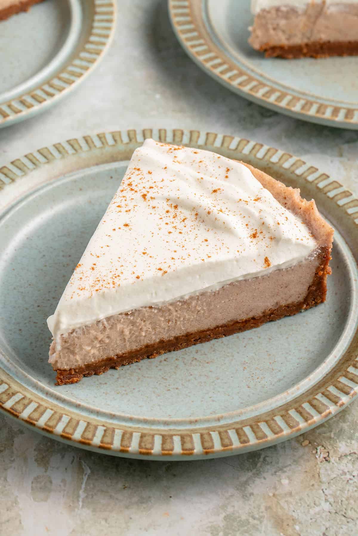 a slice of vegan chai spiced cheesecake with whipped cream and cinnamon on blue plate