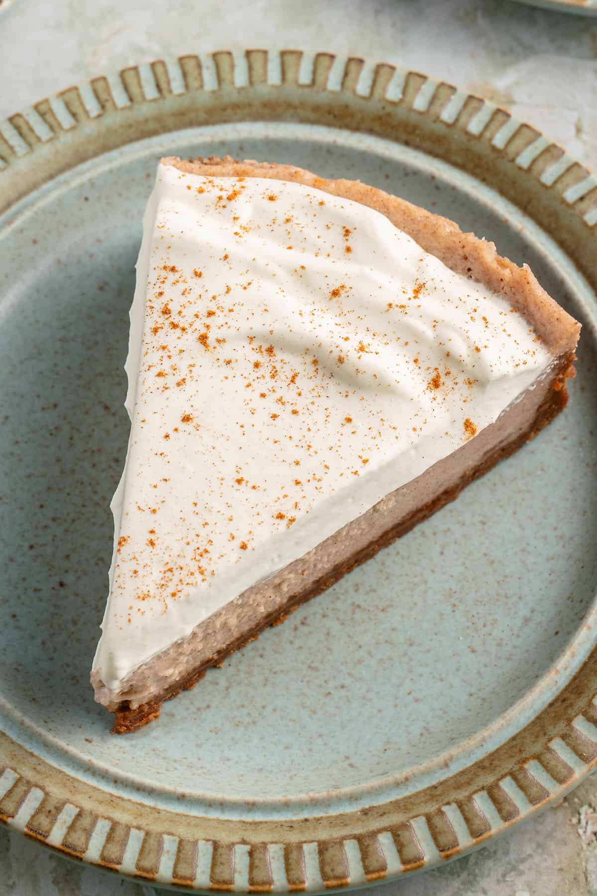 overhead photo of ova slice of vegan chai spiced cheesecake with whipped cream and cinnamon on blue plate