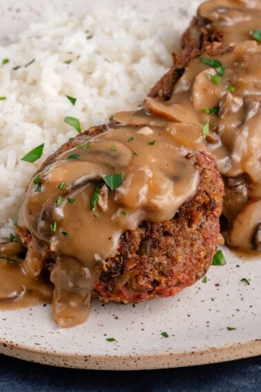 vegan filipino burger steak on a plate topped with mushroom gravy and served with rice