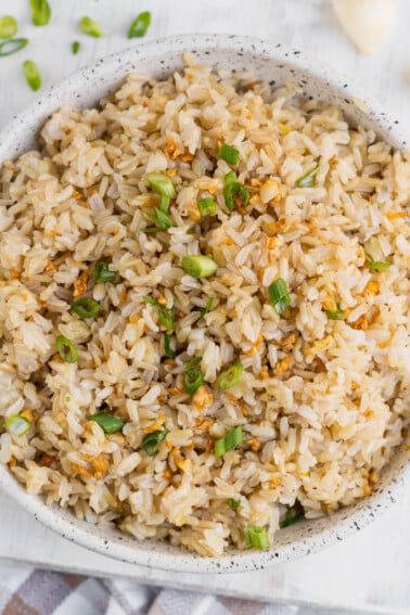 Vegan filipino garlic fried rice in a bowl with green onions and garlic on the side