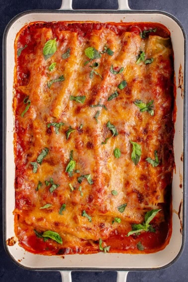 tray of baked manicotti after being baked, garnished with fresh basil