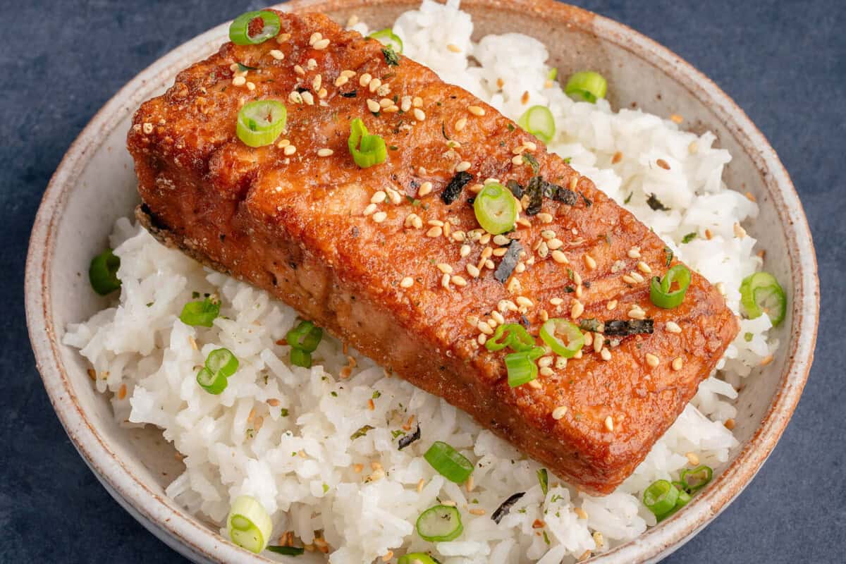 vegan salmon filet topped with green onions, sesame seeds, and seaweed on a bed of white rice