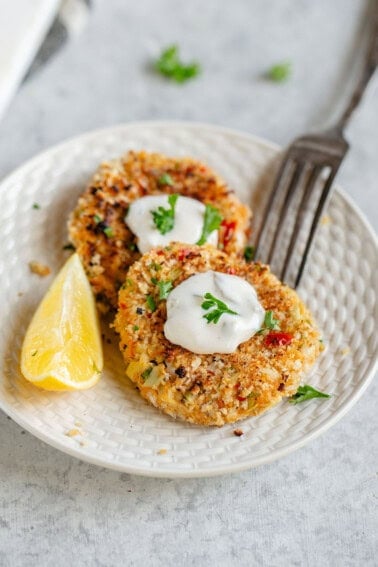 two vegan crab cakes on a plate with a dollop of tartar sauce, garnished with parsley