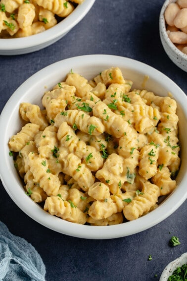 overhead photo of creamy white bean pasta with parsley in white bowl on blue background