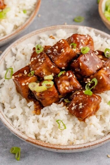 close up of saucy vegan generalo tso's tofu in a bowl with rice