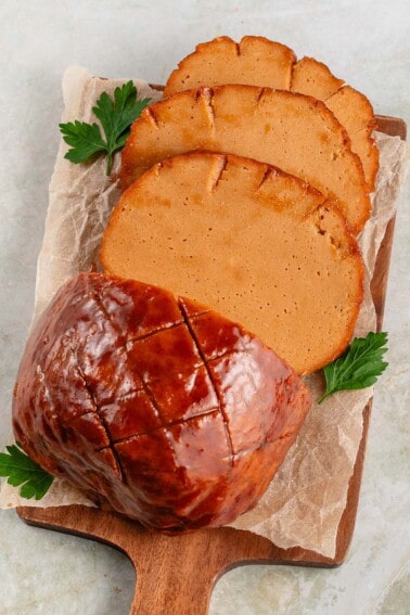 sliced vegan ham roast on parchment, garnished with parsley