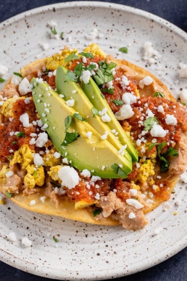 horizontal photo of vegan huevos rancheros on white plate with avocado