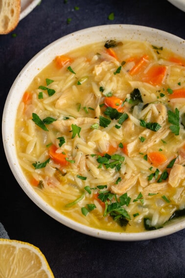 close up of lemon chicken orzo soup in white bowl on blue table